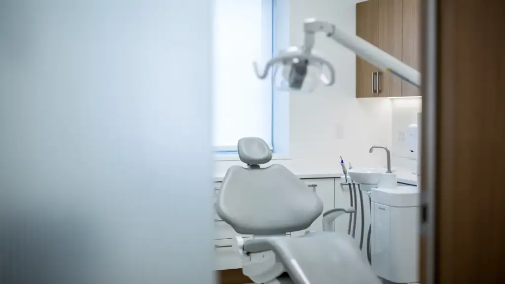 An empty treatment room seen past a frosted glass partition, the exam light swung aside