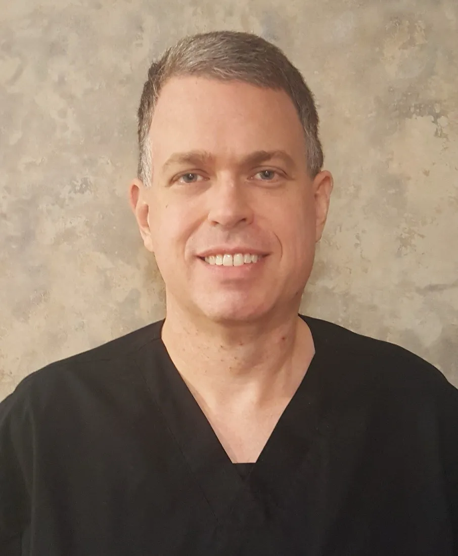 Dr. J. Matthew Cronkhite, DDS, in black scrubs against a stone-grey backdrop